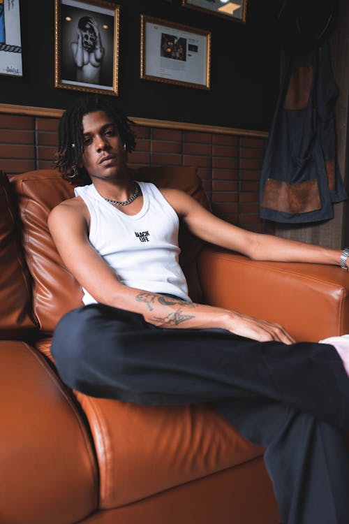Free Relaxed pensive African American male with dreadlocks resting in soft leather armchair while looking at camera Stock Photo