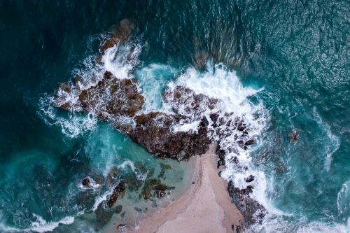 Free Dramatic aerial view of waves crashing on a rocky Greek coastline. Stock Photo