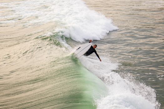 An experienced surfer skillfully rides a powerful ocean wave during sunset, showcasing agility.