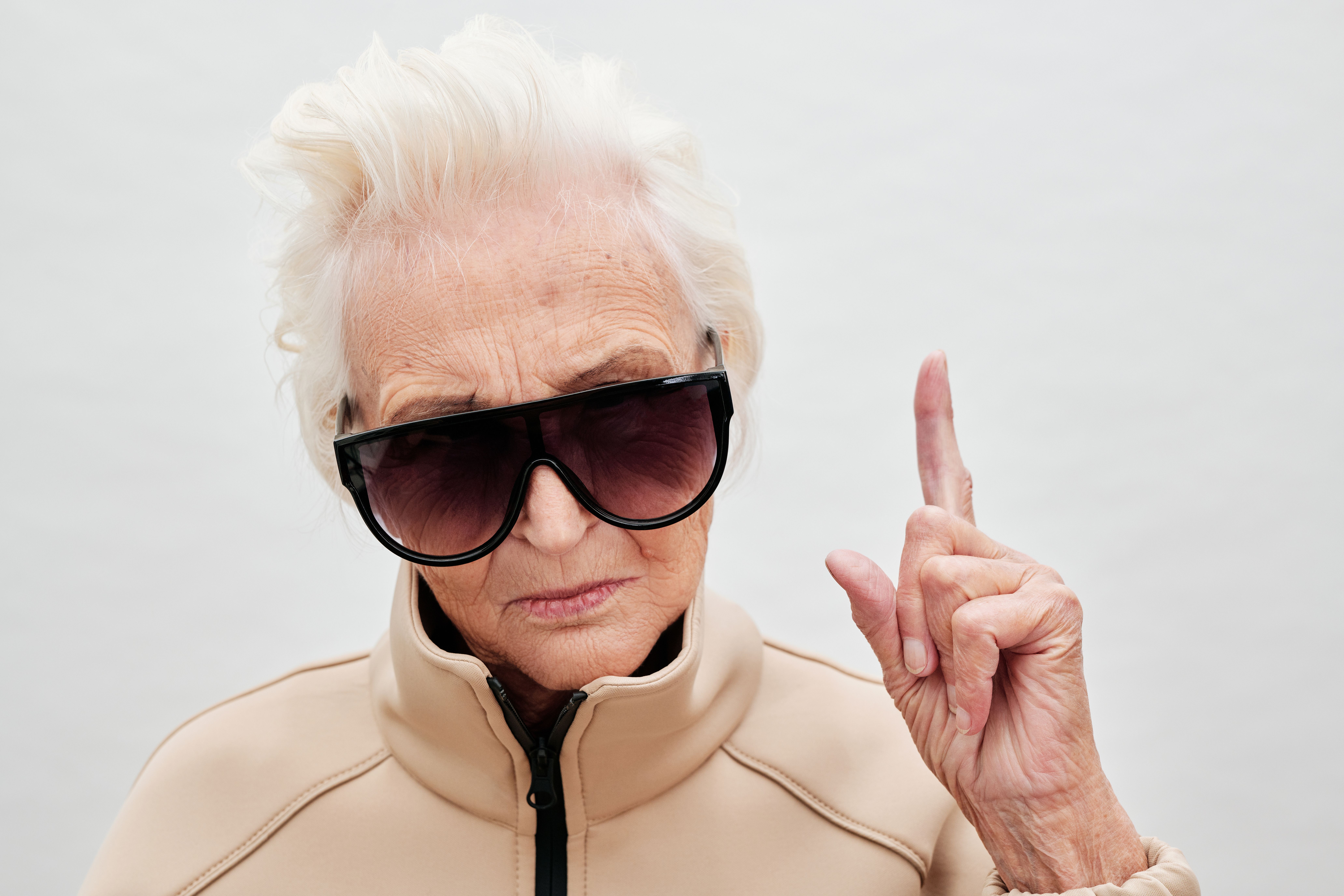 Confident senior woman wearing sunglasses, stylishly posing in a studio.