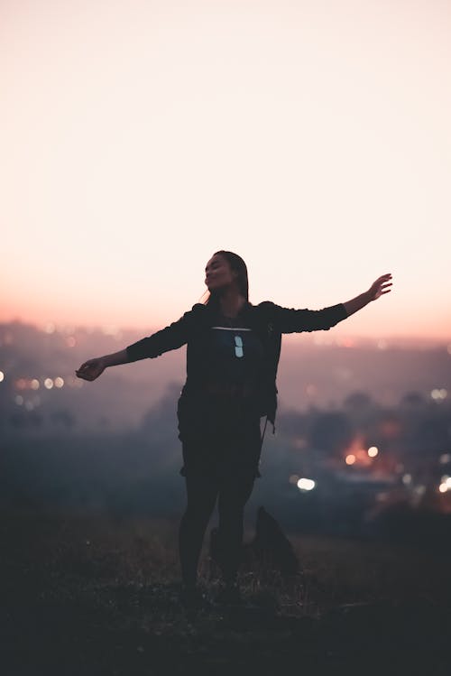 Happy black woman with arms apart on top of mountain at sunset