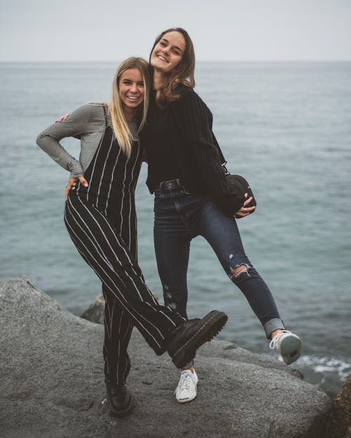 Cheerful young ladies chilling on rocky coast of ocean
