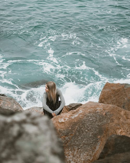 Free Woman Sitting on Rock by the Sea Stock Photo