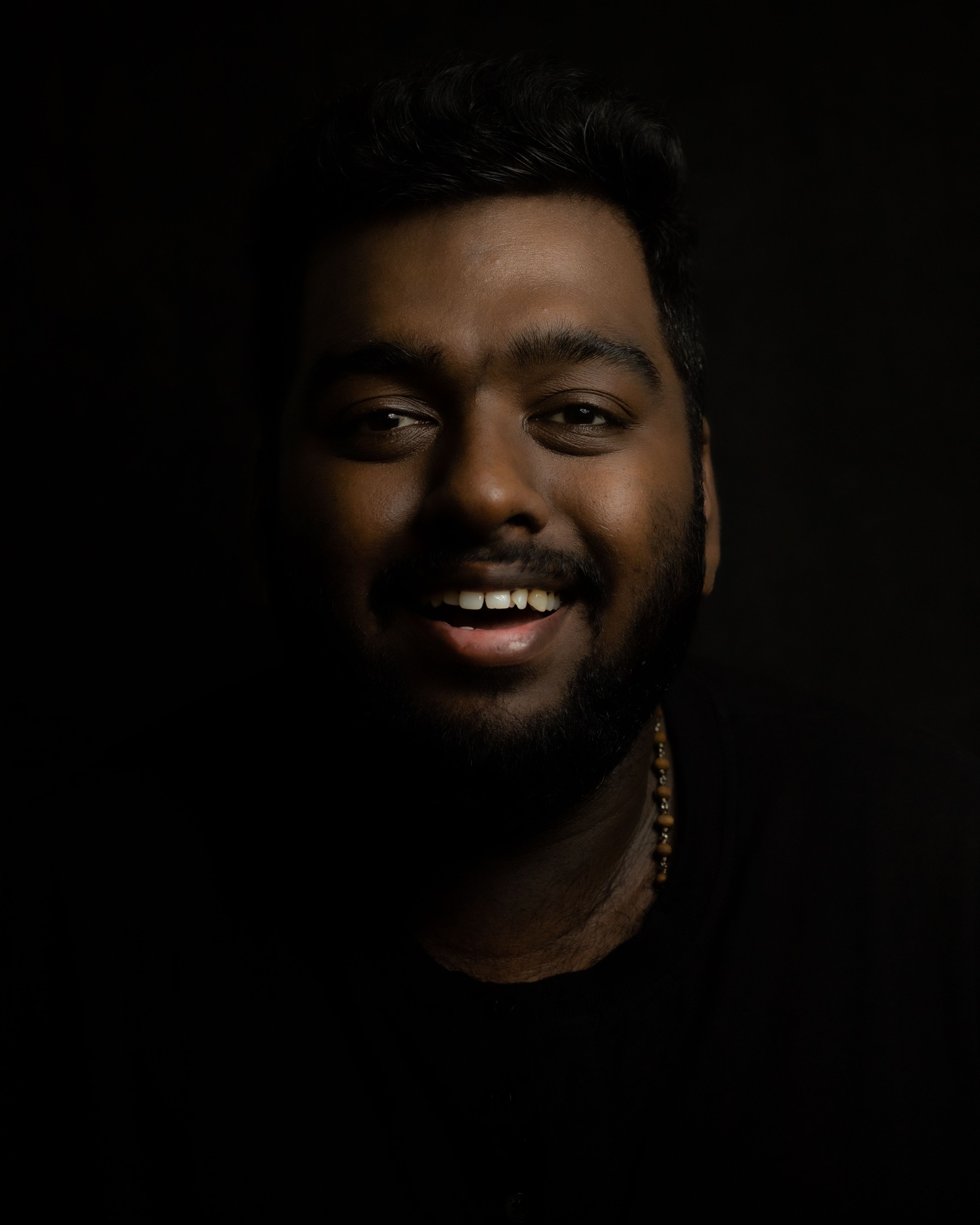 A close-up portrait of a smiling man with facial hair against a dark background.