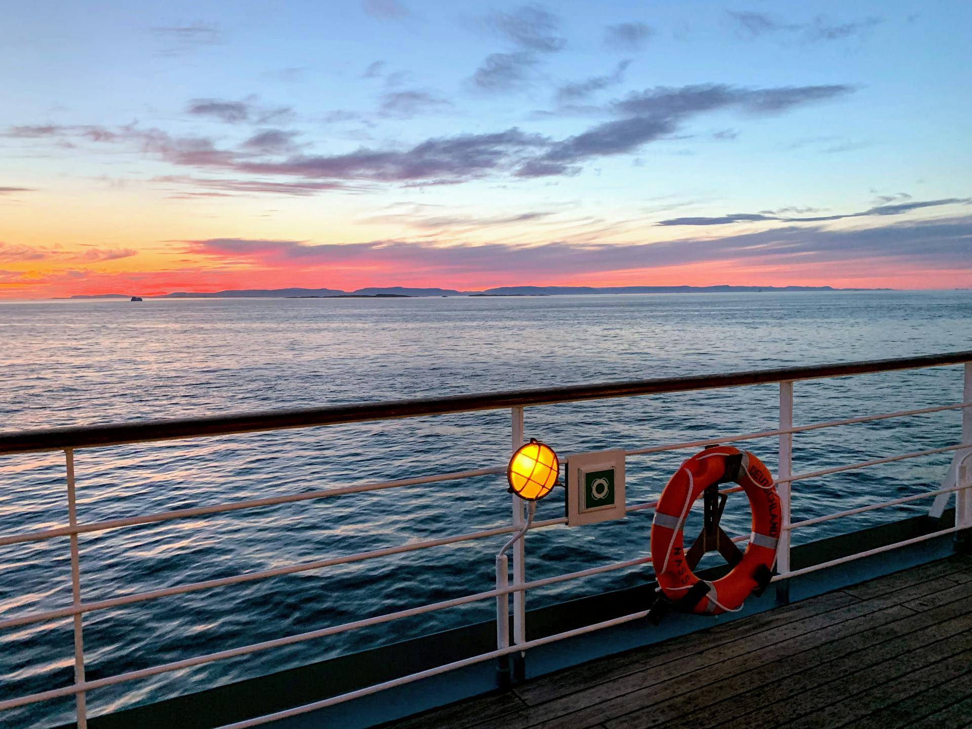 Stunning sunset from a cruise ship deck in Greenland, highlighting the calm ocean and vibrant sky.