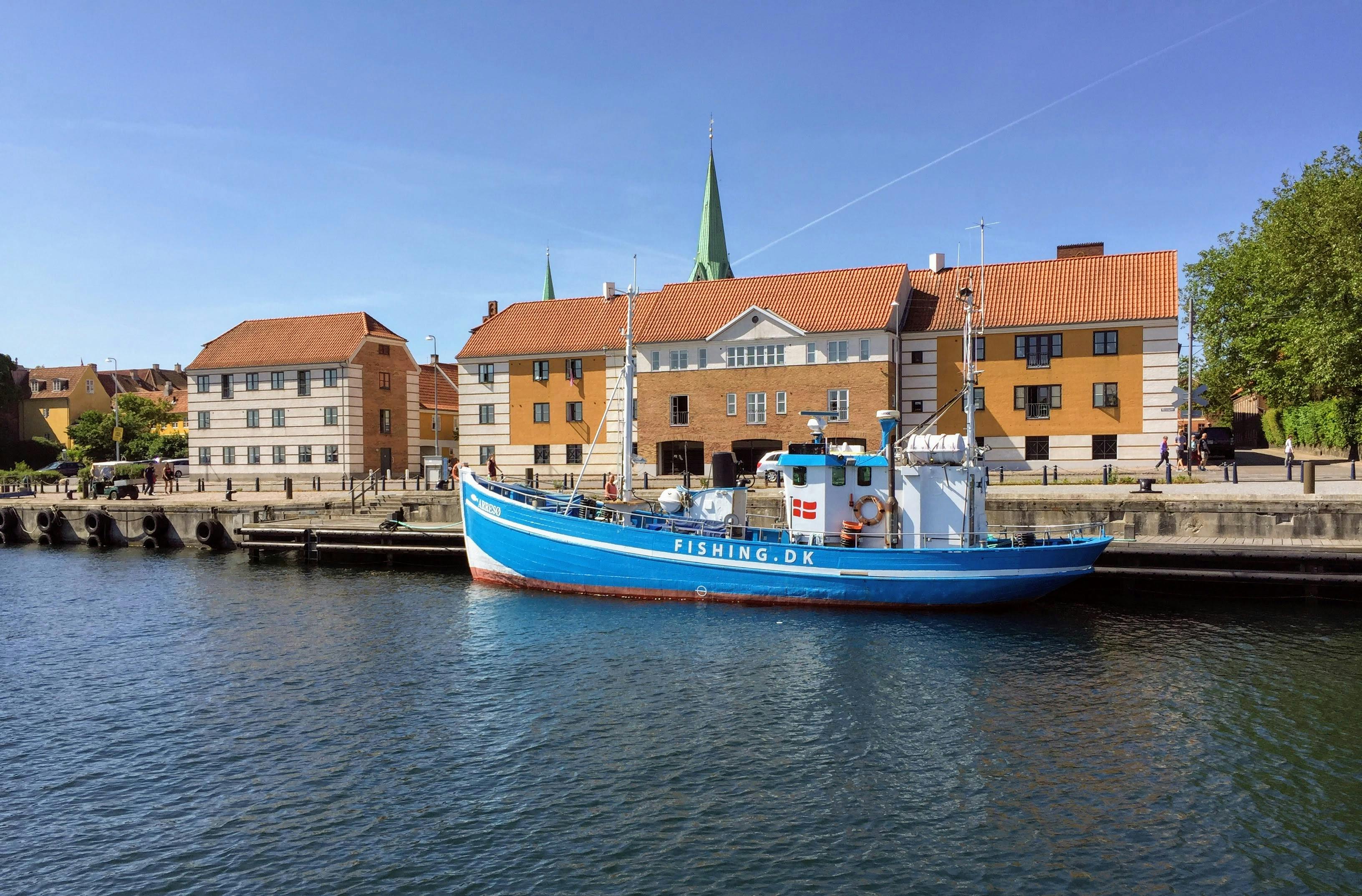 A vibrant blue fishing boat moored at Helsingør harbor with historic buildings in the background.