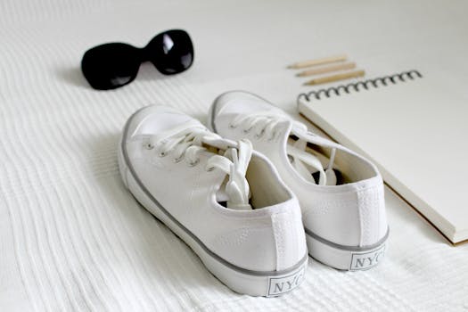 White sneakers with sunglasses and a notepad on a bed. Minimalist style.