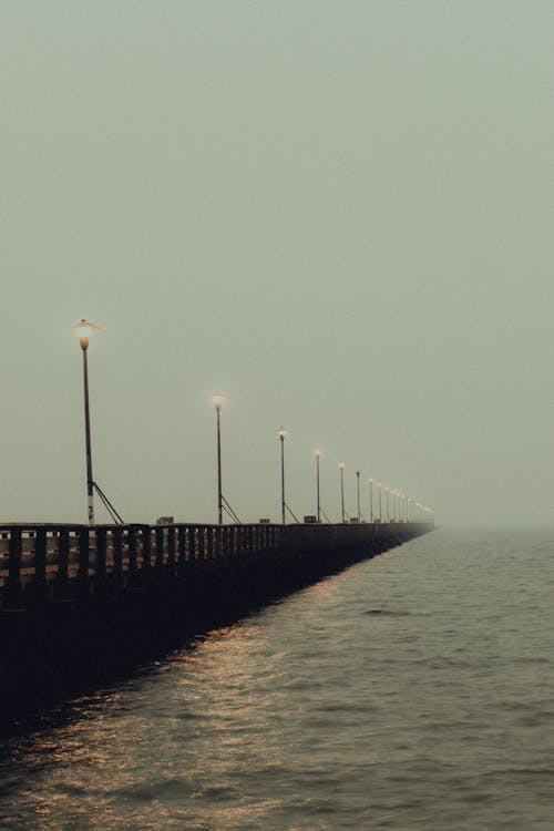 Long pier near rippling water of river on cloudy misty weather in summer