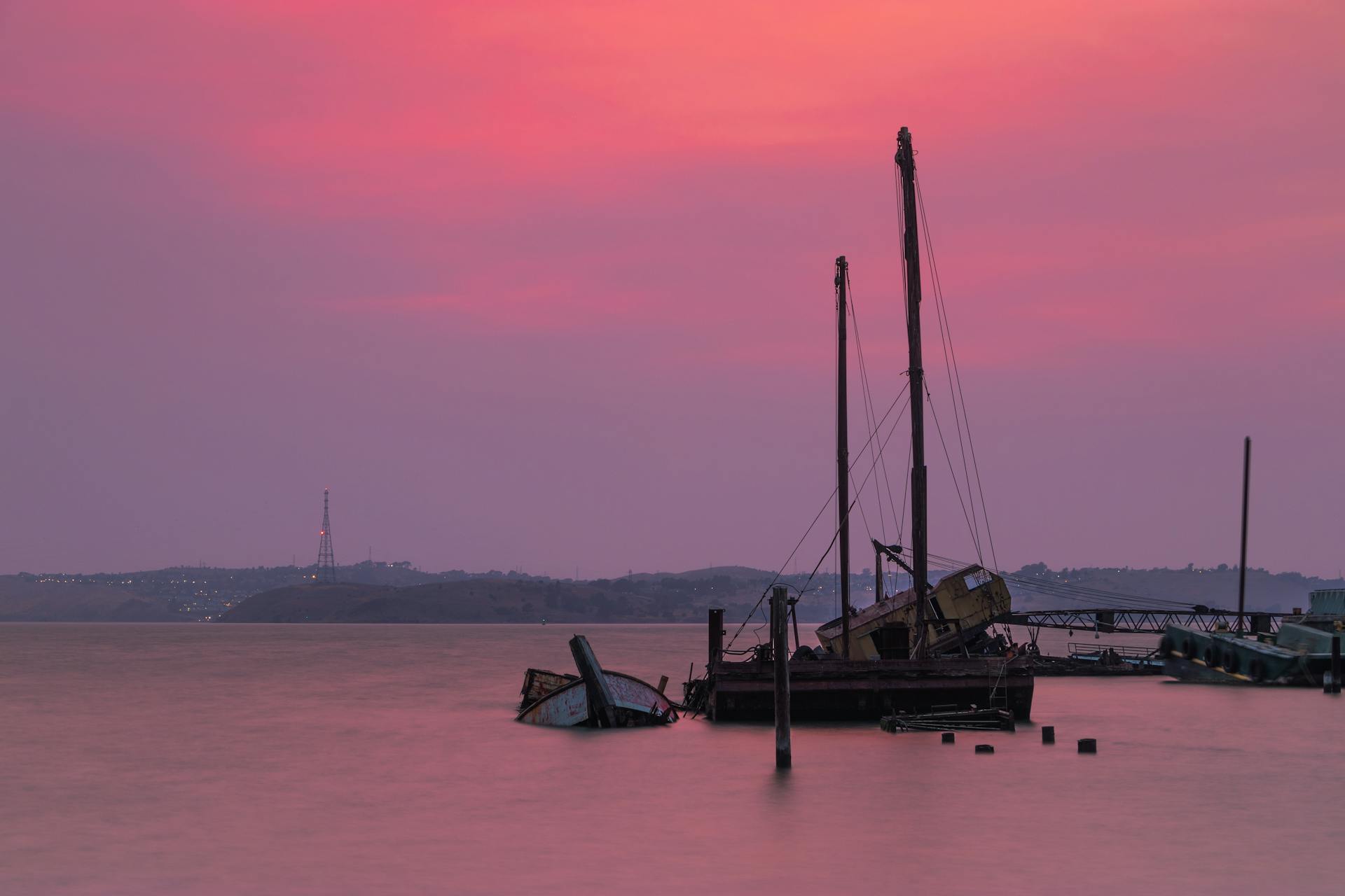 Picturesque abandoned vessels floating near aged pier and hills on purple cloudy sunset