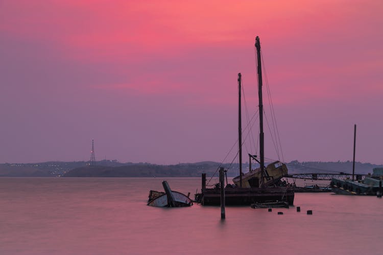 Sinking Boat Near Old Pier On Bright Sunset