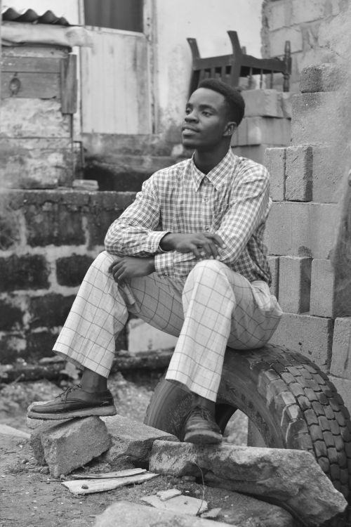 Free Black and white photo of a man in checkered shirt sitting outdoors on a tire. Stock Photo