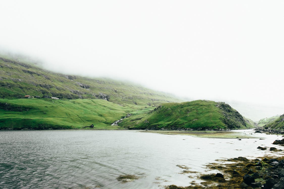 Free Green Grass Covered Mountain Beside Body of Water Stock Photo