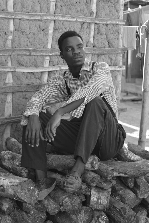 Free Black and white image of an adult man in a checkered shirt sitting on firewood. Stock Photo