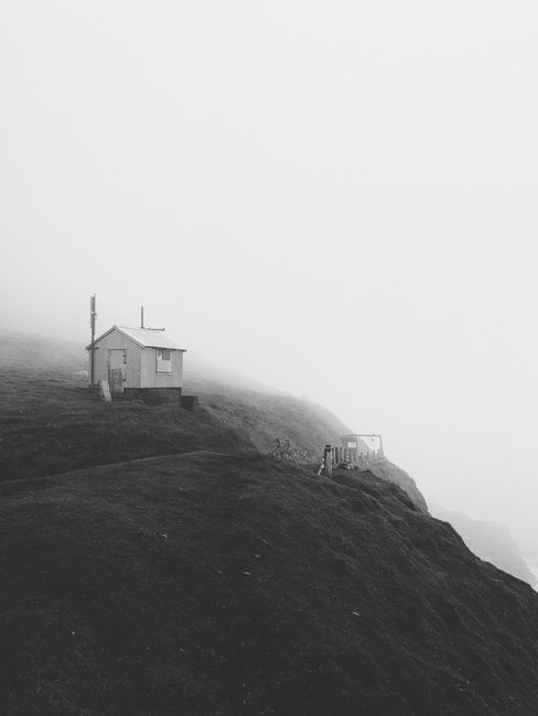 A misty landscape with a solitary house on a cliff in the Faroe Islands.