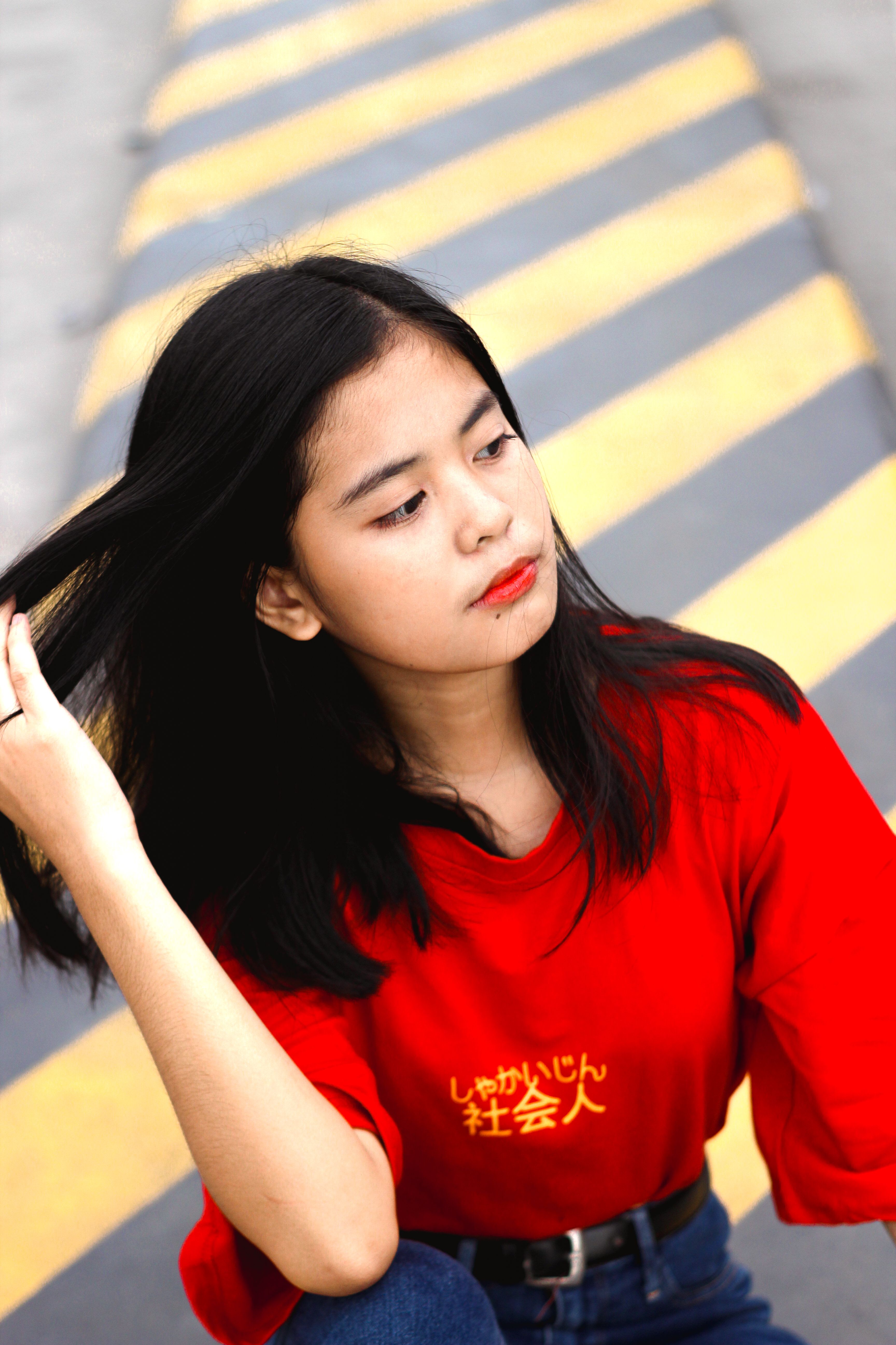 Portrait of a young woman in a red shirt with urban background holding her hair.