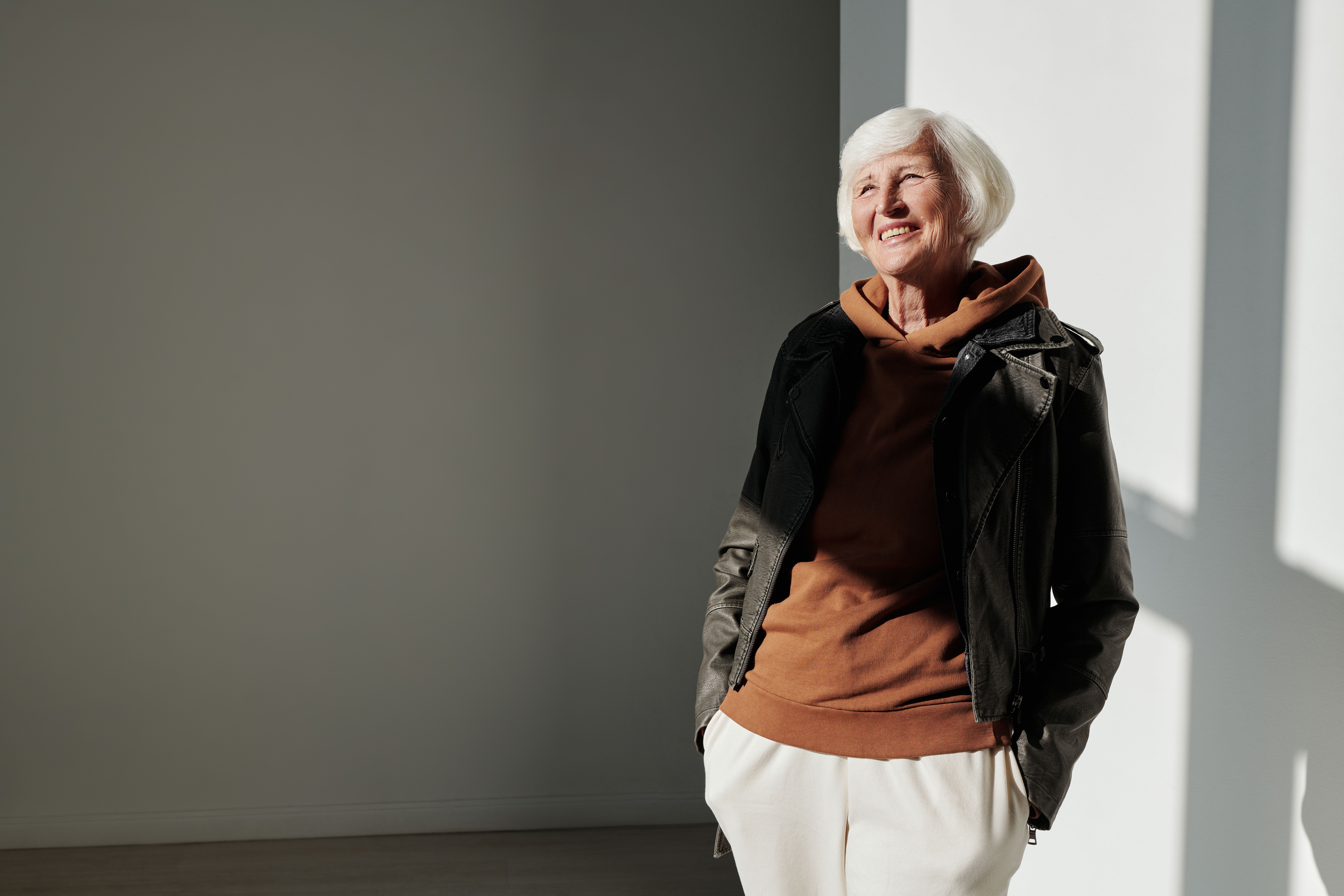 Senior woman exudes confidence in trendy leather jacket indoors with sunlight.