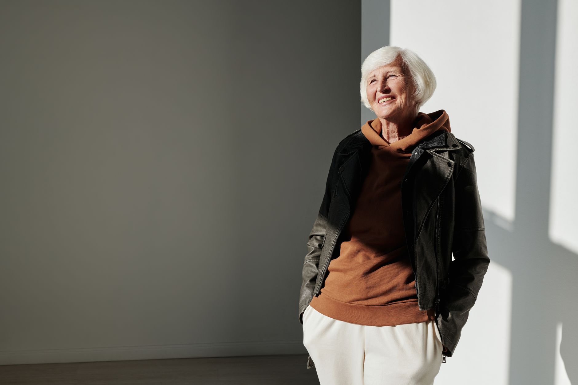 Senior woman exudes confidence in trendy leather jacket indoors with sunlight.