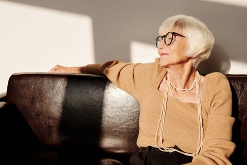 Free Elderly Woman in Brown Long Sleeve Shirt Wearing Eyeglasses Sitting on Black Couch Stock Photo