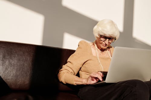 Elderly Woman in Brown Long Sleeve Shirt Using Laptop