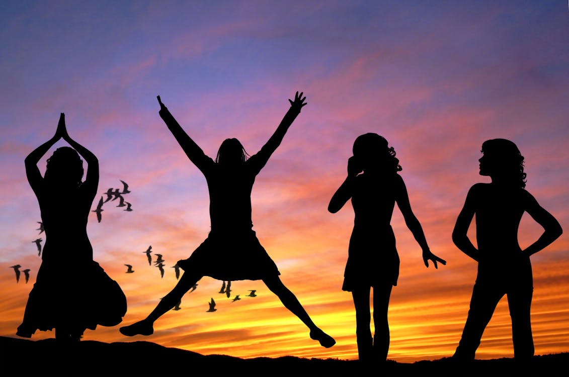 Free Silhouette of 4 Women With the Background of Birds Flying Under Yellow and Grey Sky Stock Photo