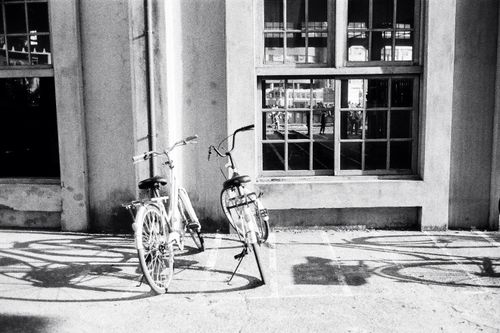 Free Black and white of vintage bikes placed on paved sidewalk near stone building at daytime Stock Photo