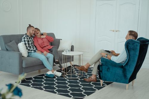 Free A happy couple enjoying a light moment in a therapy session with a therapist indoors. Stock Photo