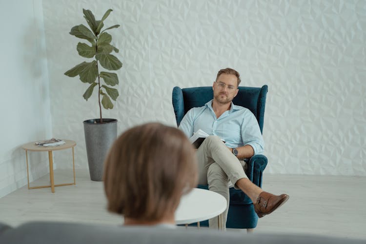 A Man Sitting On A Blue Sofa Chair In Front Of A Person