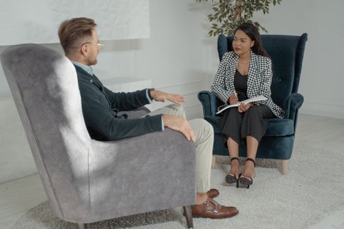 Free Two professionals conducting an interview in a modern office with stylish chairs and a white backdrop. Stock Photo
