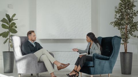 A therapist and patient engaged in conversation in a modern, stylish therapy office.