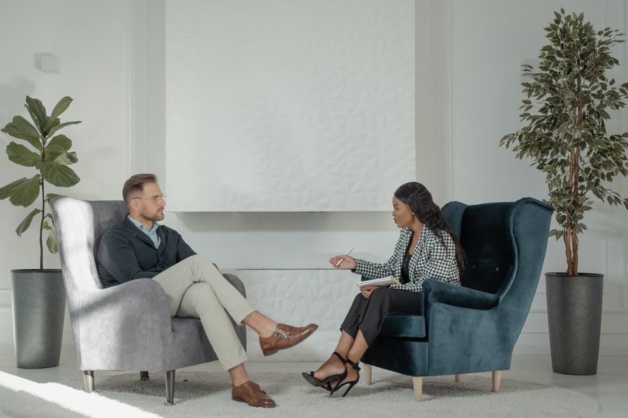 Two people seated in armchairs during a consultation in a plant-filled room. Photo by Tima Miroshnichenko on Pexels