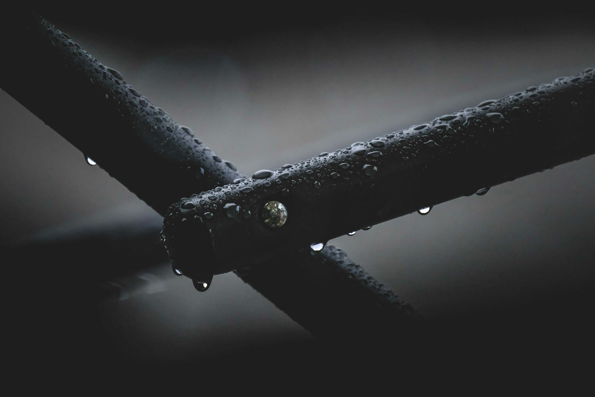 Closeup of black metal pipes covered in water drops and attached with nail