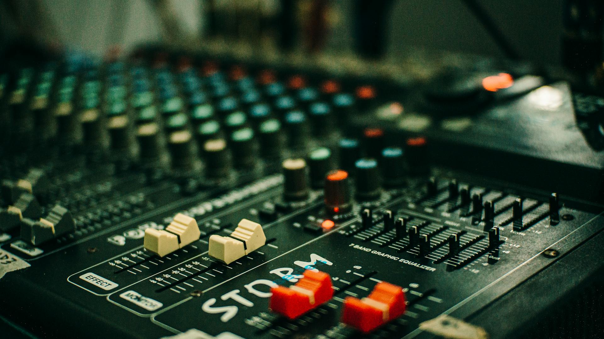 Detailed view of a sound mixer with knobs and sliders in a studio setting.