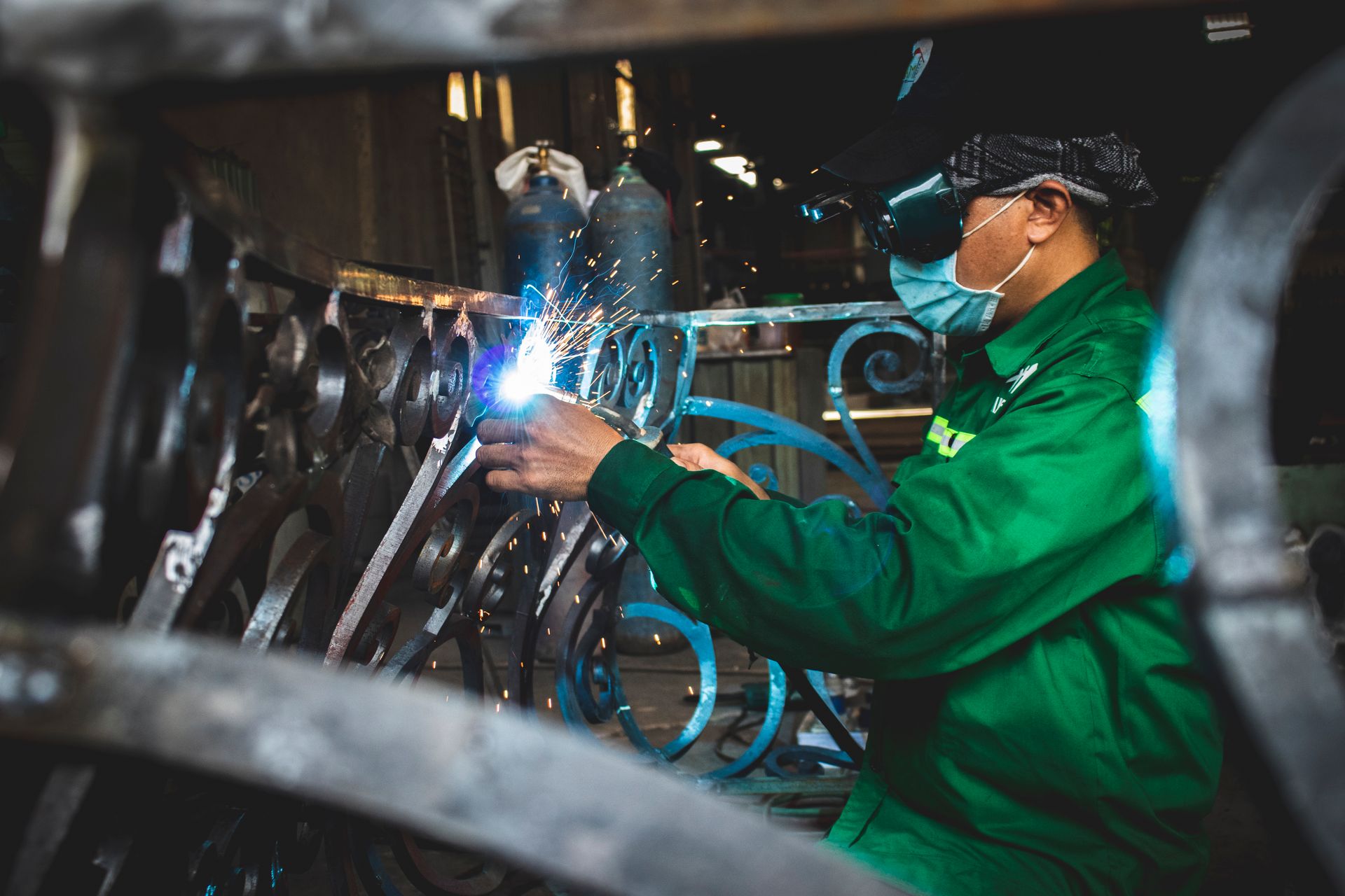 Welder in protective gear working on metal with torch indoors, showcasing industrial skill.