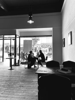 Black and white of faceless male and female chilling at table next to picture window in cozy time cafe