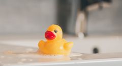 Close-up of a yellow rubber duck floating in a bathtub with soap bubbles.