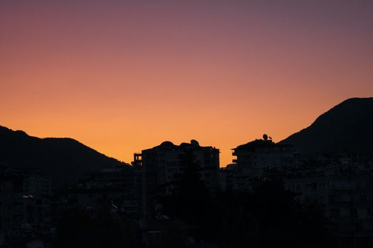 Stunning silhouette of city buildings against a vivid sunset sky, framed by mountains.