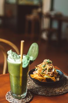 A refreshing green smoothie with bamboo straw beside a savory snack on a wooden table indoors.