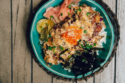 Free Colorful poke bowl with rice, fish, and fresh vegetables presented on a rustic wooden table. Stock Photo