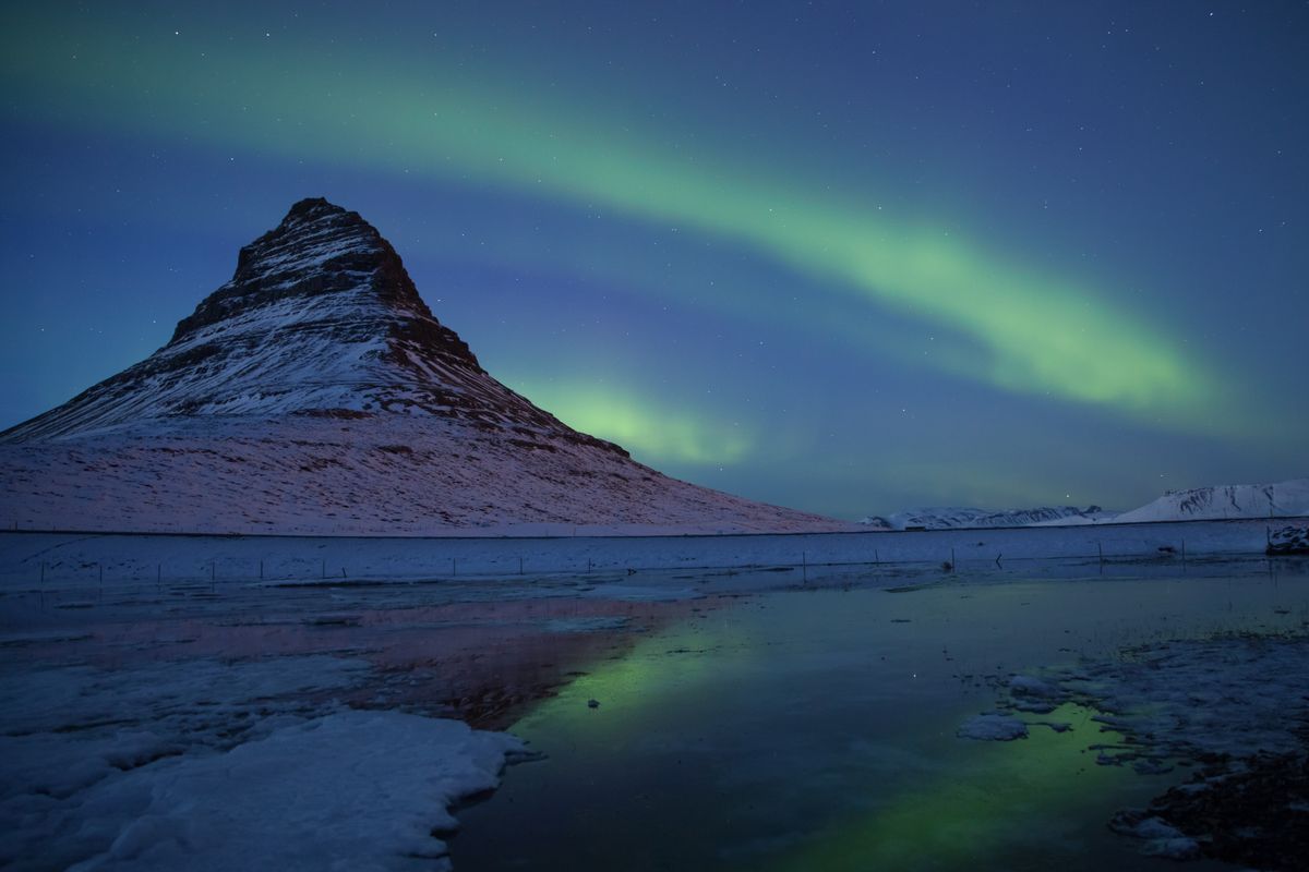 Aurora boreală verde deasupra muntelui Kirkjufell, oglindită într-un lac înghețat, Islanda