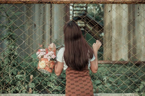 Back view of young faceless female standing near fence and trying to find way through it