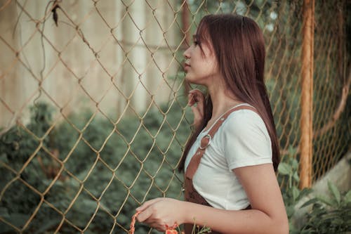 Free Side view of young female thinking on escape while standing near fence in countryside Stock Photo