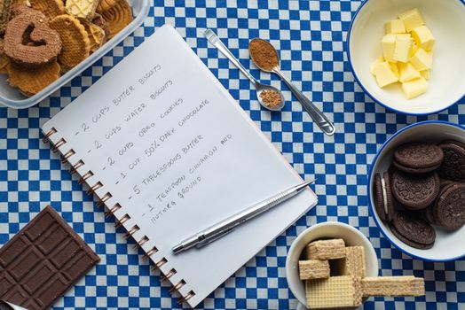Flat lay of dessert ingredients and recipe on a checkered tablecloth with cookies and chocolate.