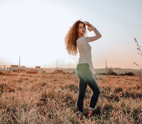 Woman in White Top and Blue Denim Jeans Posing on a Grass Field
