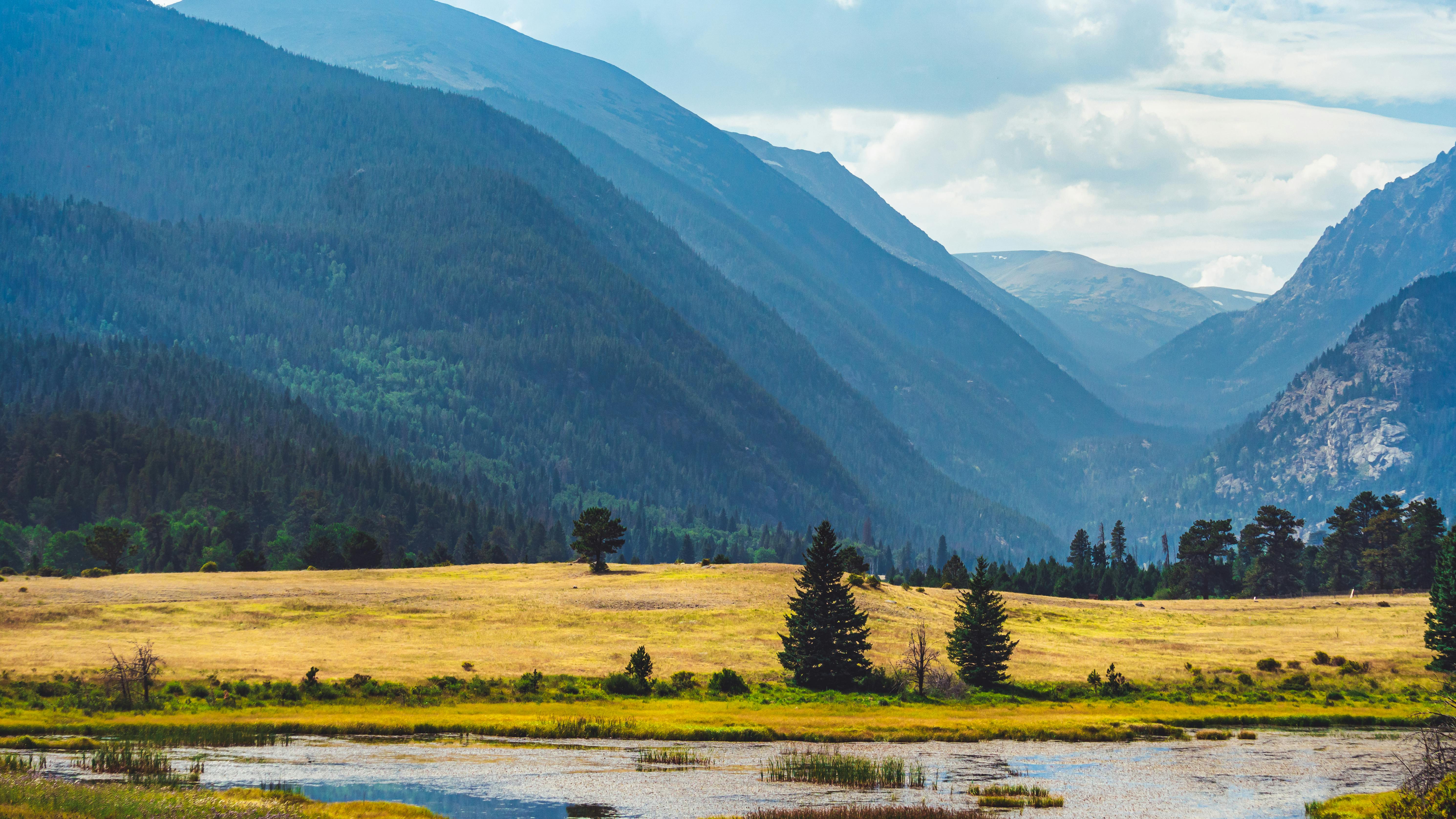 Scenic view of rolling mountains, fields, and forests under a cloudy sky.