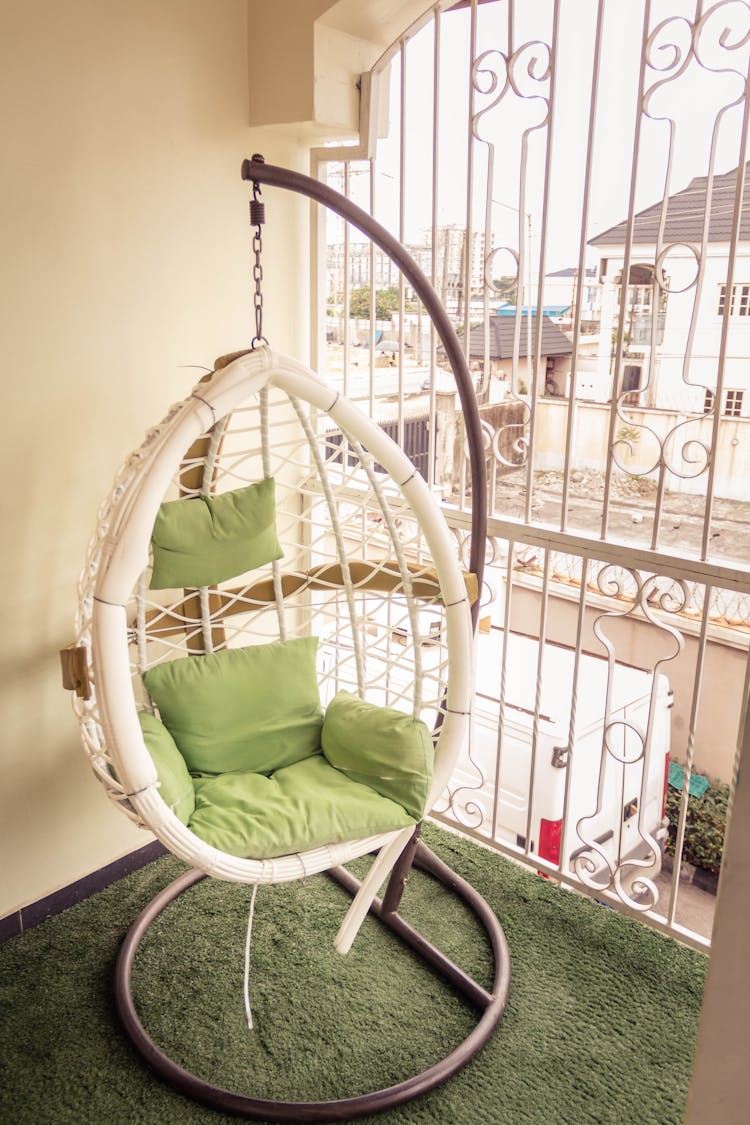 A White Cocoon Chair Wit Green Cushions In The Balcony