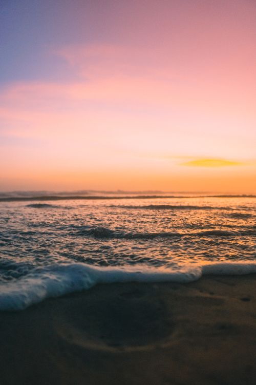 Free Peaceful sunset over the ocean with waves gently lapping on the sandy beach. Stock Photo