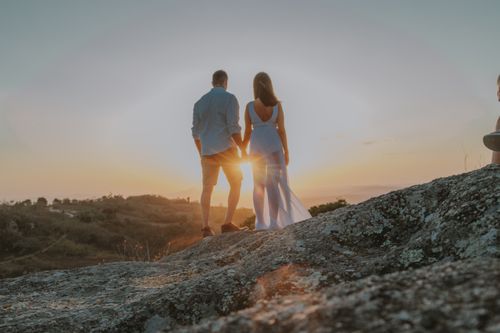 Free A couple holding hands on a rocky hill at sunset, embracing love and togetherness. Stock Photo