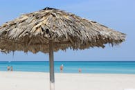 在原始热带海滩上，碧绿的海水边，打着稻草伞放松身心