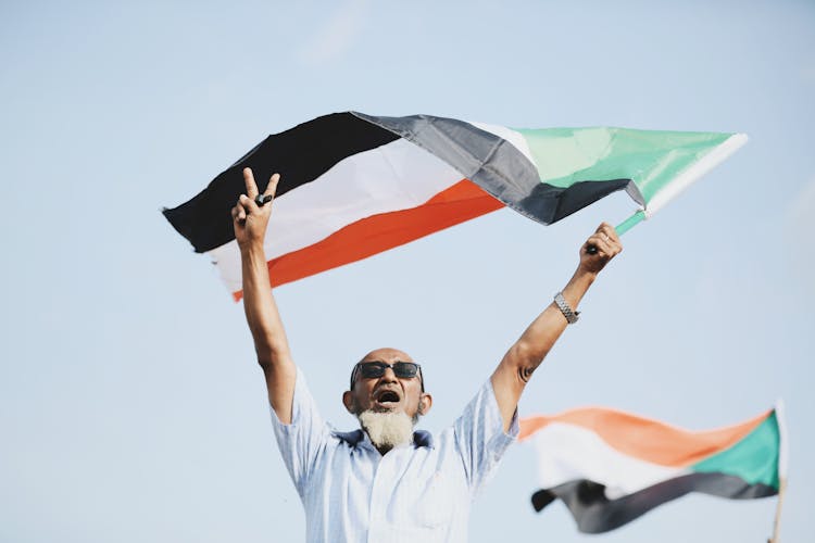 Man In Button Up Shirt Waving Sudanese Flag In Victory