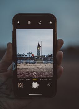 Photo of a clock tower framed on a smartphone screen held by a hand.